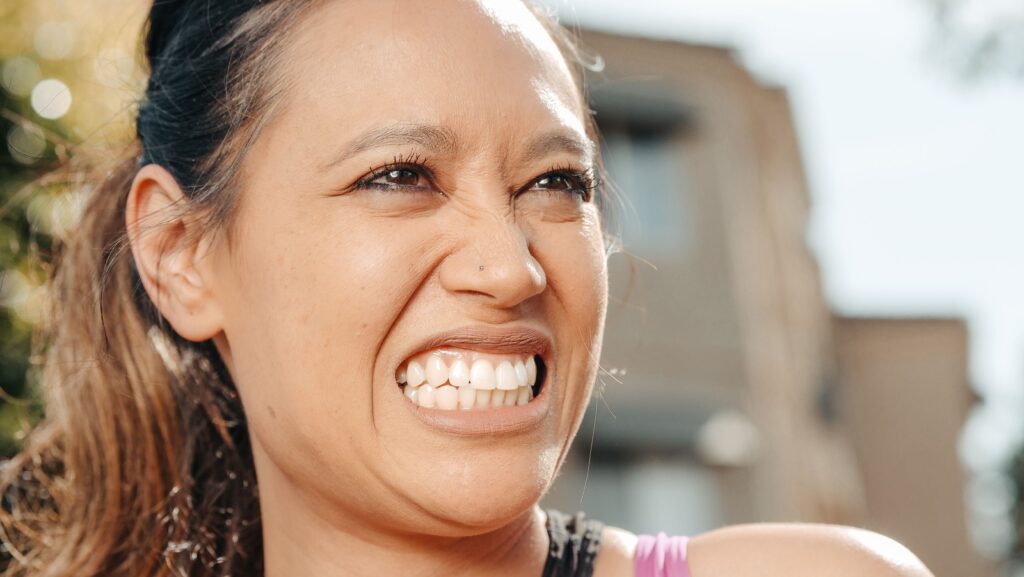 Vibrant close-up of a woman smiling outdoors on a sunny day.