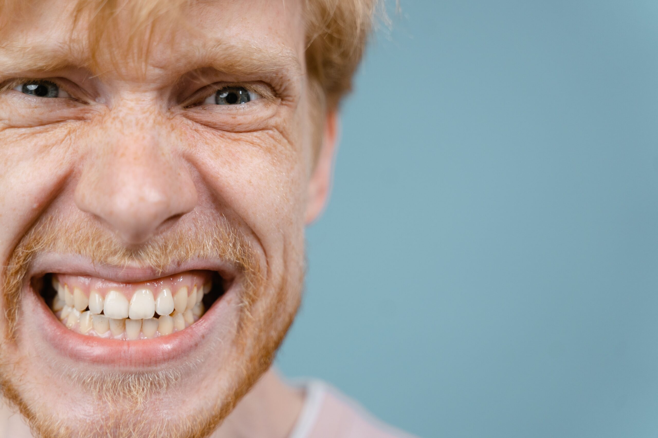 A close-up portrait of a man with a wacky and intense facial expression against a blue background.