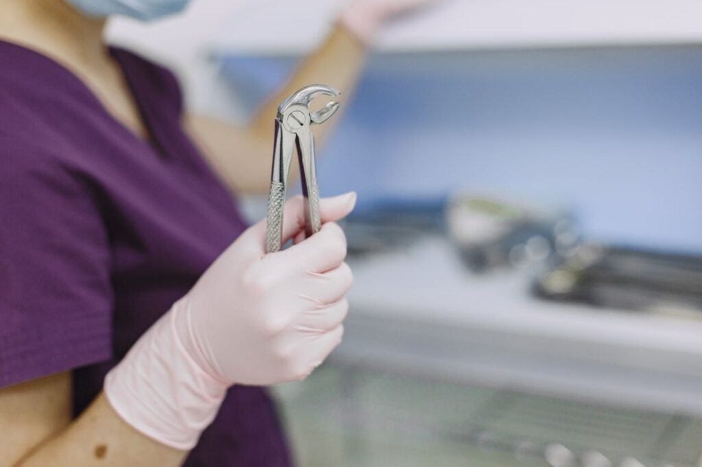 Close-up of a dentist's hand holding extraction forceps in a sterile dental clinic environment.