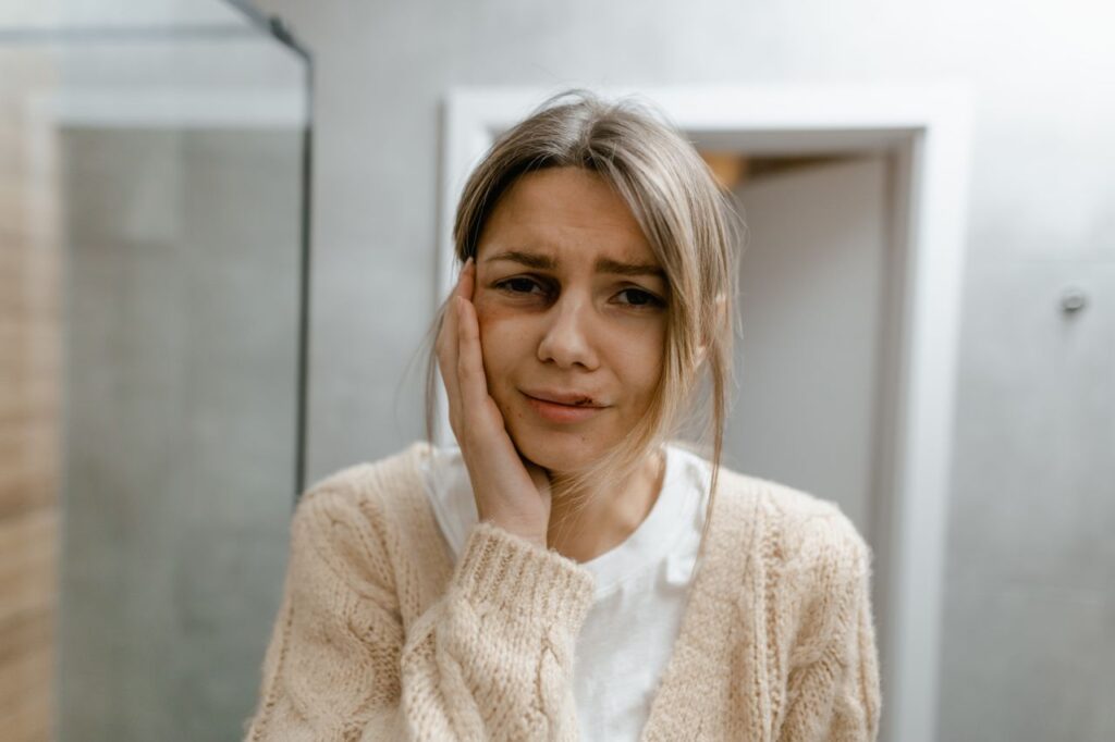 A worried woman stands indoors, touching her face, displaying signs of discomfort.